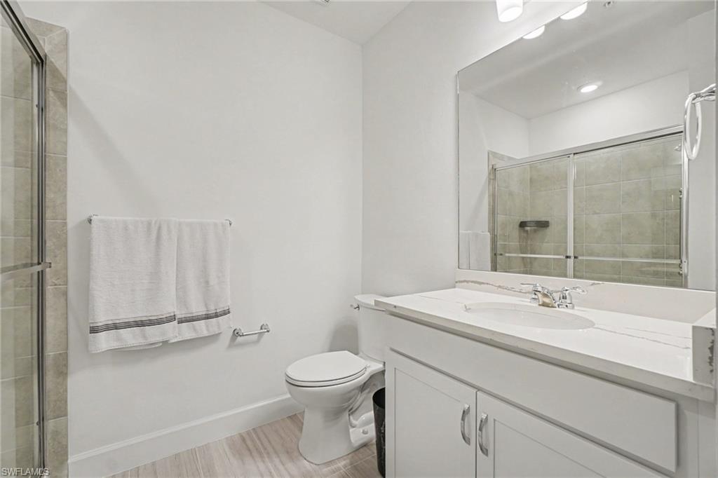 Bathroom featuring a vanity with a white countertop and undermount sink, a large mirror, a shower with sliding glass doors and tiled surround, and wood-finish flooring