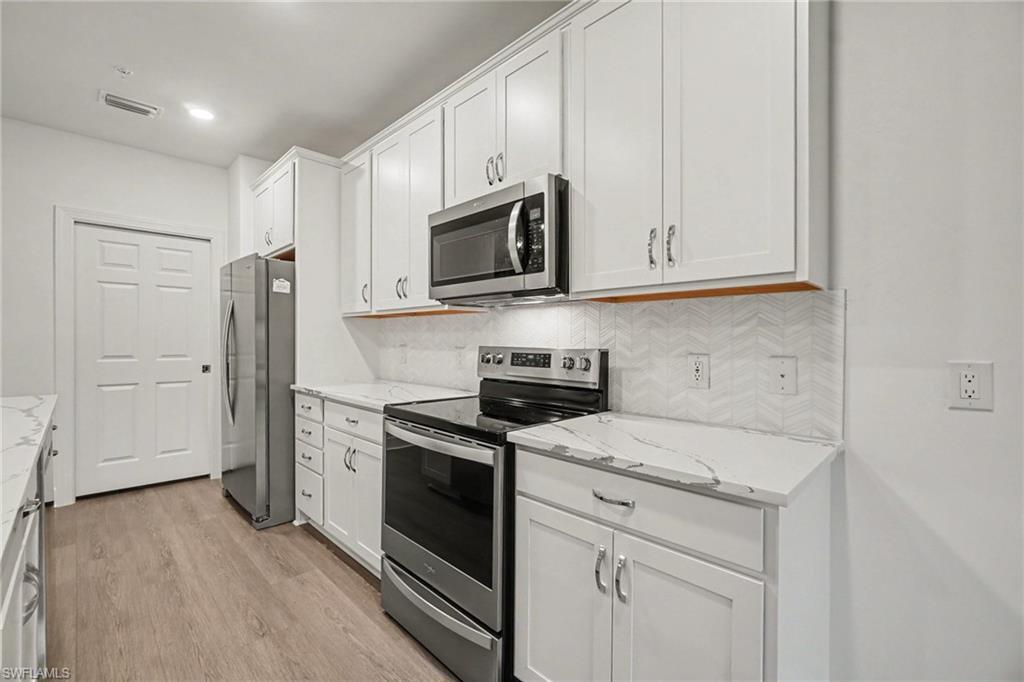 Kitchen featuring white shaker-style cabinetry, stainless steel appliances, marble-look countertops, a herringbone pattern tile backsplash, and wood-finish flooring