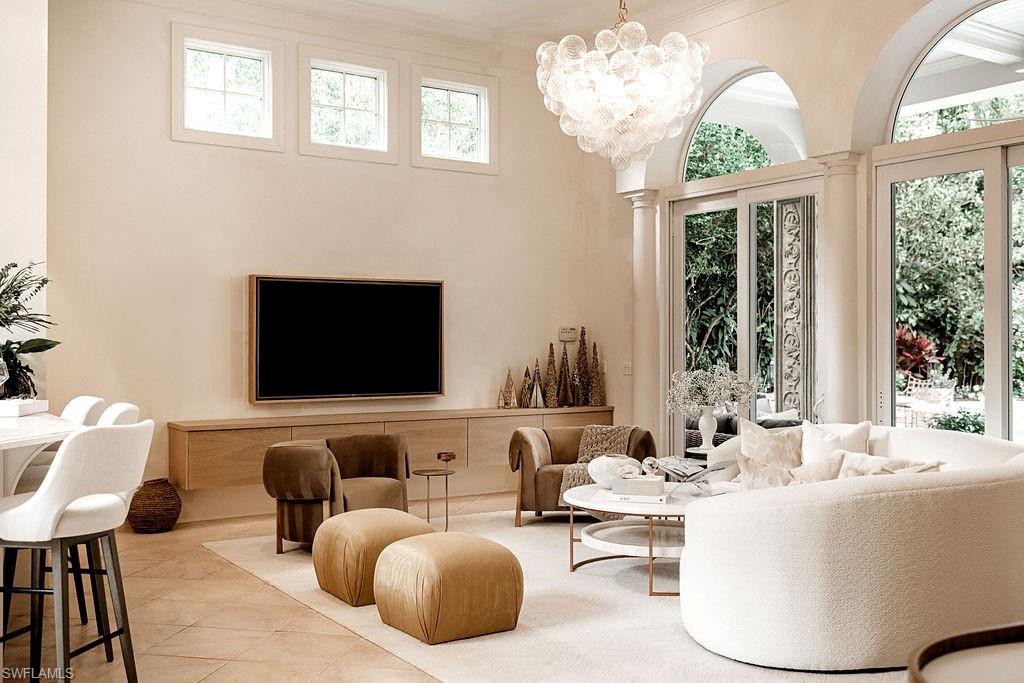 Spacious living area featuring high ceilings, a contemporary bubble chandelier, and abundant natural light from arched windows and glass doors
