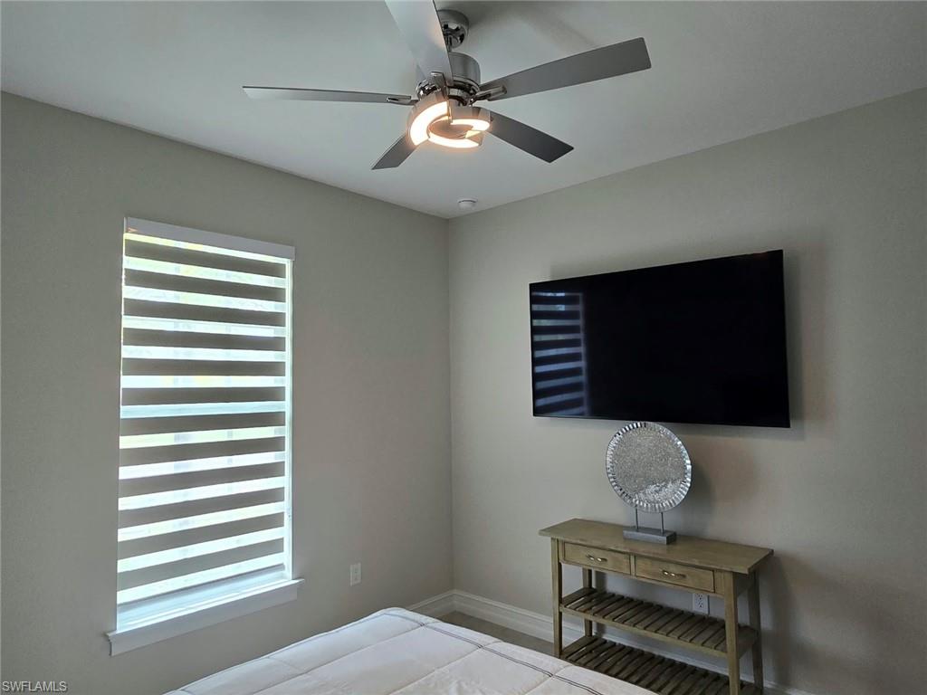 Wall-mounted television with a console table, ceiling fan with integrated lighting, and window with banded shades