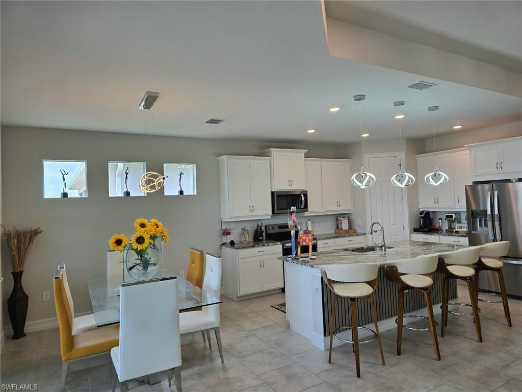 Kitchen featuring white cabinetry, stainless steel appliances, a large island with built-in sink, and pendant lighting