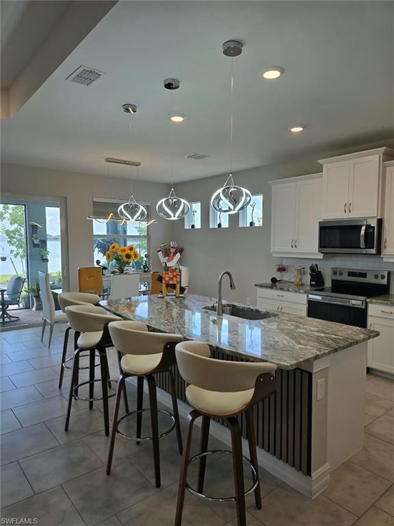 Expansive kitchen island with a stone countertop and integrated sink, stainless steel appliances, white cabinetry, and tile flooring