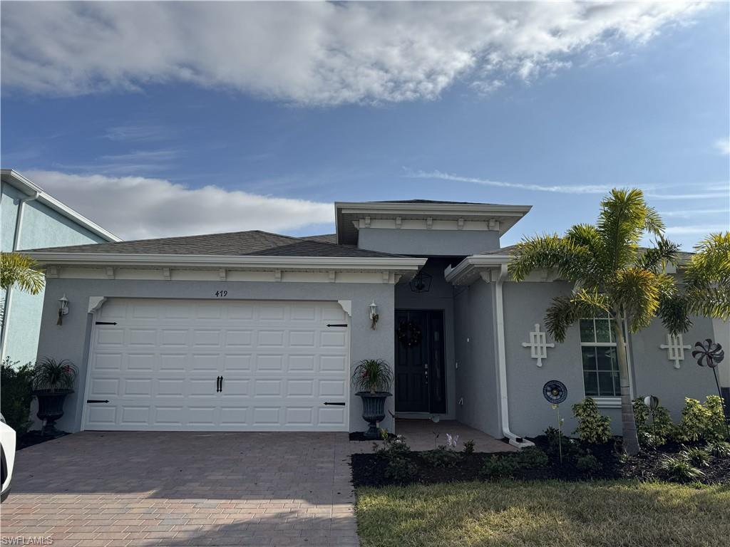 Single-story residence featuring a gray exterior with white trim, a dark asphalt shingle roof, a paver driveway, and a two-car garage with decorative hardware