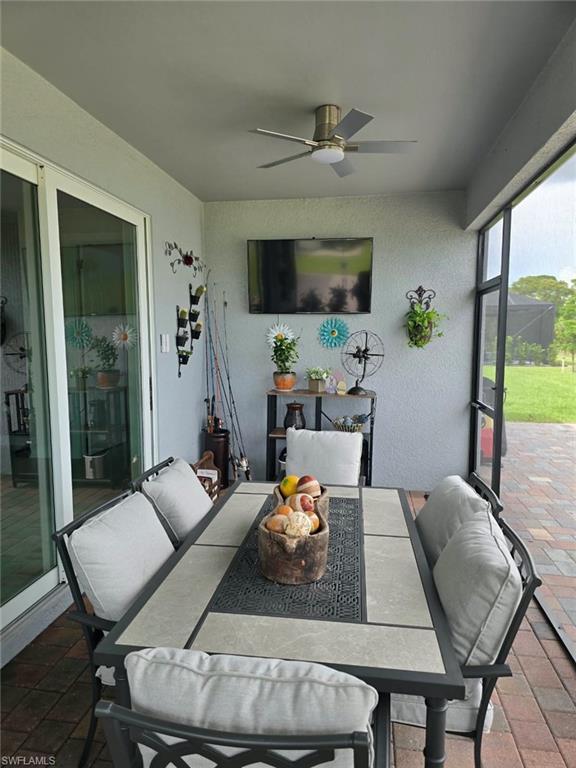 Screened outdoor living area featuring a ceiling fan, wall-mounted television, and sliding glass doors