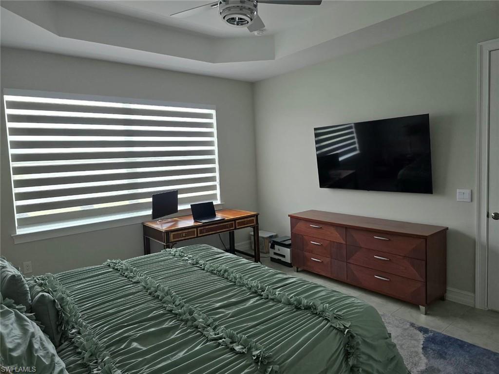 Recessed tray ceiling, ceiling fan, window with horizontal blinds, wall-mounted display, and light-toned wall paint