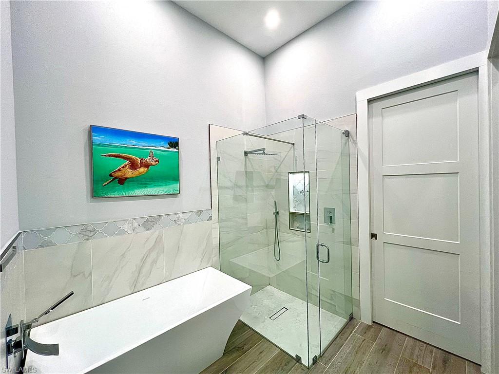 Contemporary bathroom featuring a frameless glass shower enclosure, a built-in shower niche, a freestanding soaking tub with a floor-mounted faucet, and wood-finish flooring