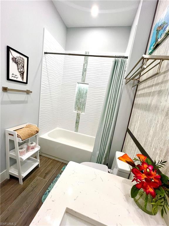Bathroom featuring a shower-tub combination with textured white tile surround, an accent vertical tile stripe, and wood-finish flooring