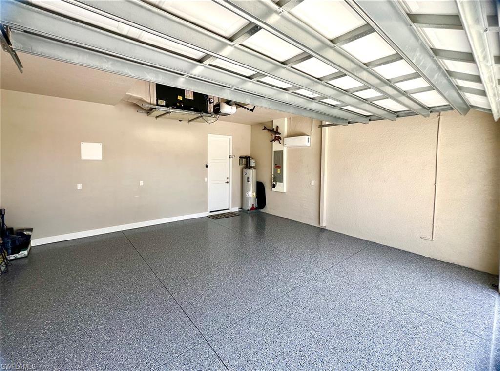 Spacious garage with an epoxy-coated concrete floor, white interior access door, and a wall-mounted air conditioning unit