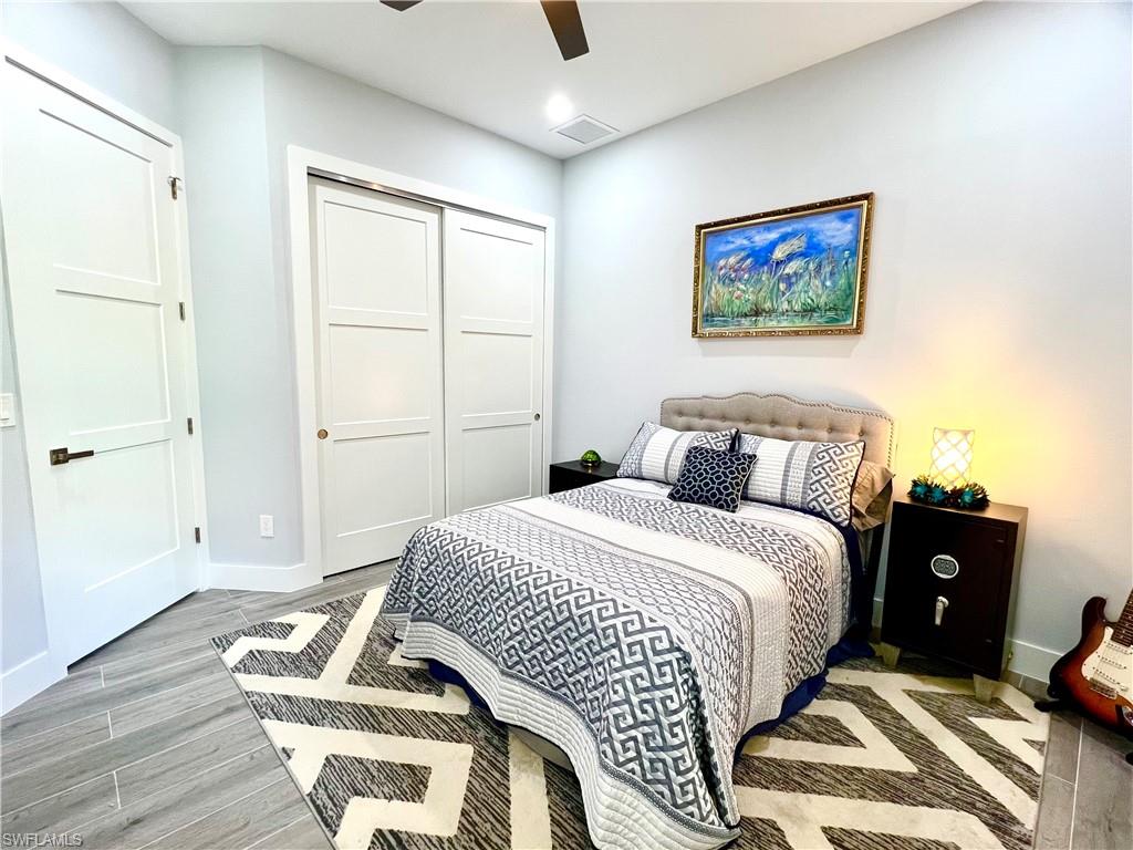 Bedroom featuring light wood-finish flooring, a contemporary ceiling fan, three-panel interior doors with dark hardware, and sliding closet doors
