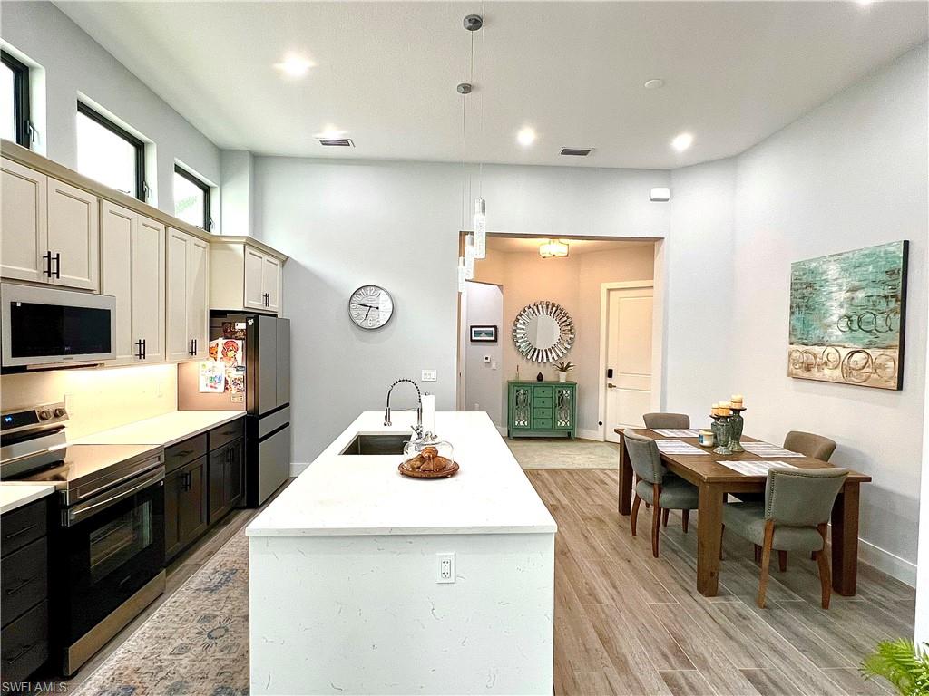Spacious kitchen featuring an expansive island with an undermount sink and a stainless steel faucet, stainless steel appliances, and a dining area with wood-finish flooring
