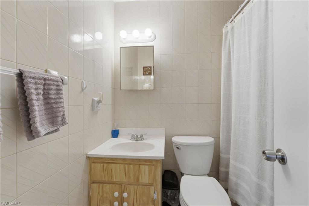 Bathroom featuring full-height tile walls, a vanity with a wood-finish cabinet and integrated sink, a wall-mounted medicine cabinet with overhead lighting, and a toilet
