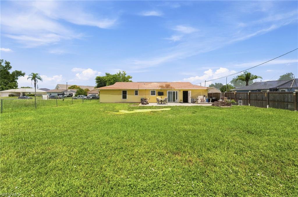 Expansive grassy backyard featuring a paved patio, sliding glass doors, a privacy fence, and an additional storage structure