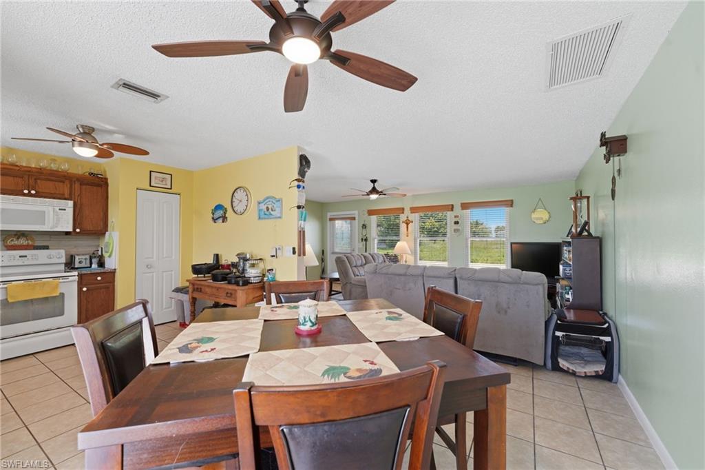 Open-concept living area with tile flooring throughout, featuring a kitchen with wood cabinetry and white appliances, a dining area, and a living room with multiple windows