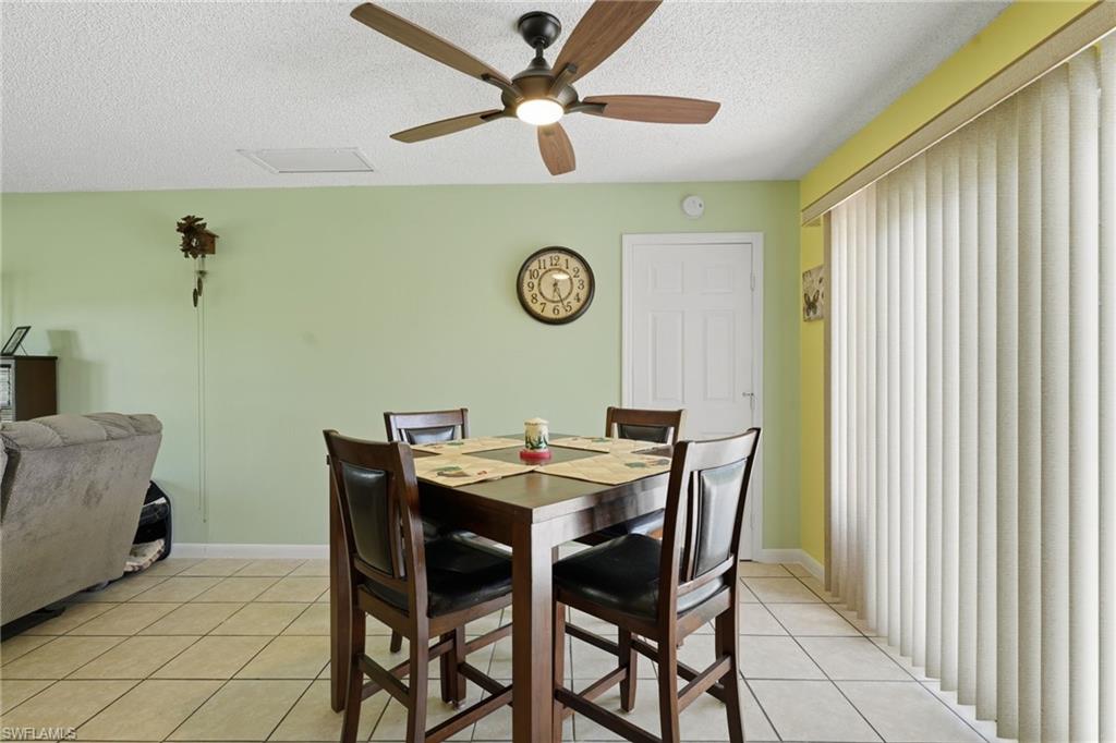 Tiled flooring throughout this open space, featuring a ceiling fan with integrated lighting, a panel door, and vertical blinds on the patio door