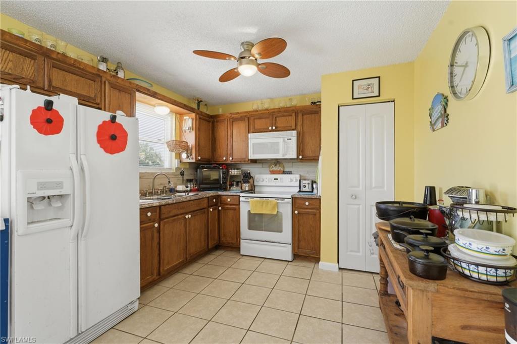 Kitchen featuring wood cabinetry, light-toned countertops, white appliances, and a ceiling fan with integrated lighting
