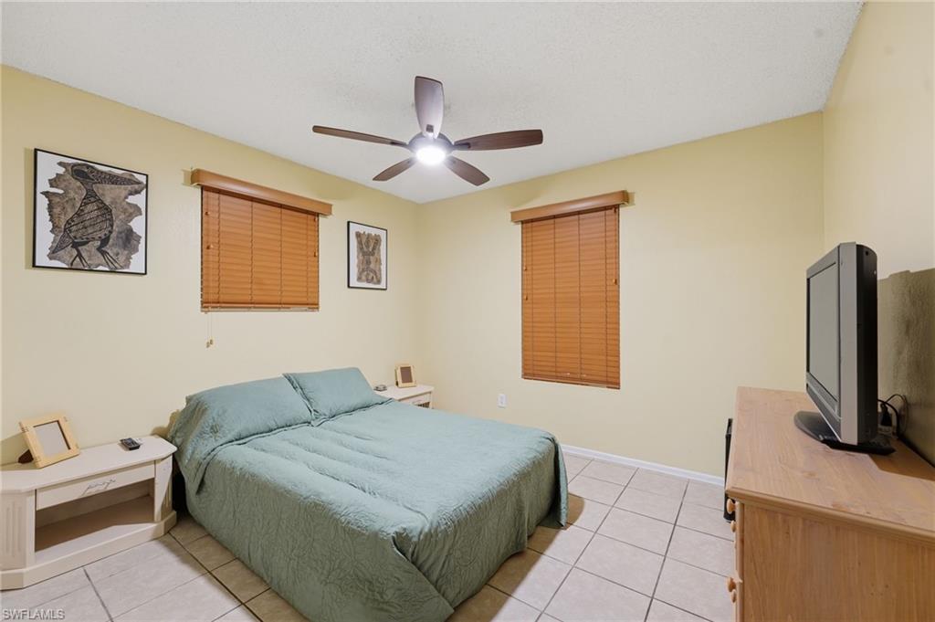 Bedroom featuring ceramic tile flooring, two windows with wood-finish blinds, a ceiling fan with integrated lighting, and neutral wall tones