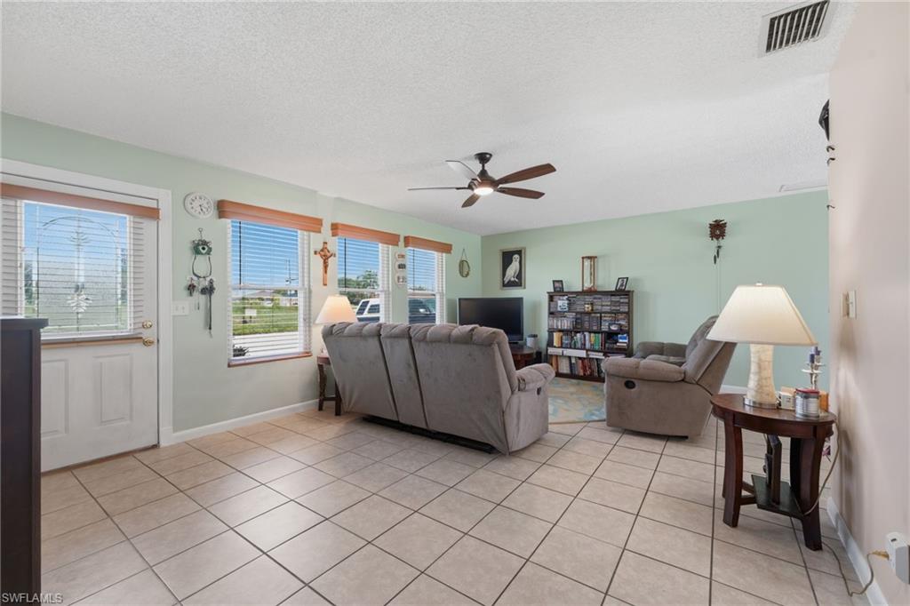 Living area featuring light-colored tile flooring, multiple windows with blinds, a ceiling fan fixture, and light green wall tones