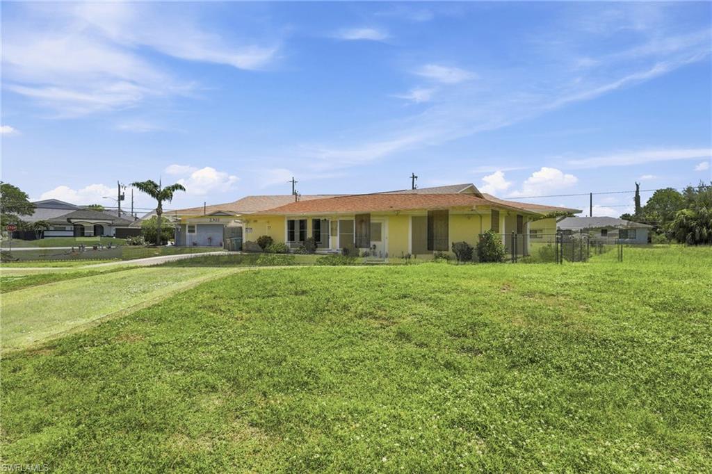 Spacious corner lot featuring a single-story residence with a yellow exterior, brown shingle roof, and a paved driveway