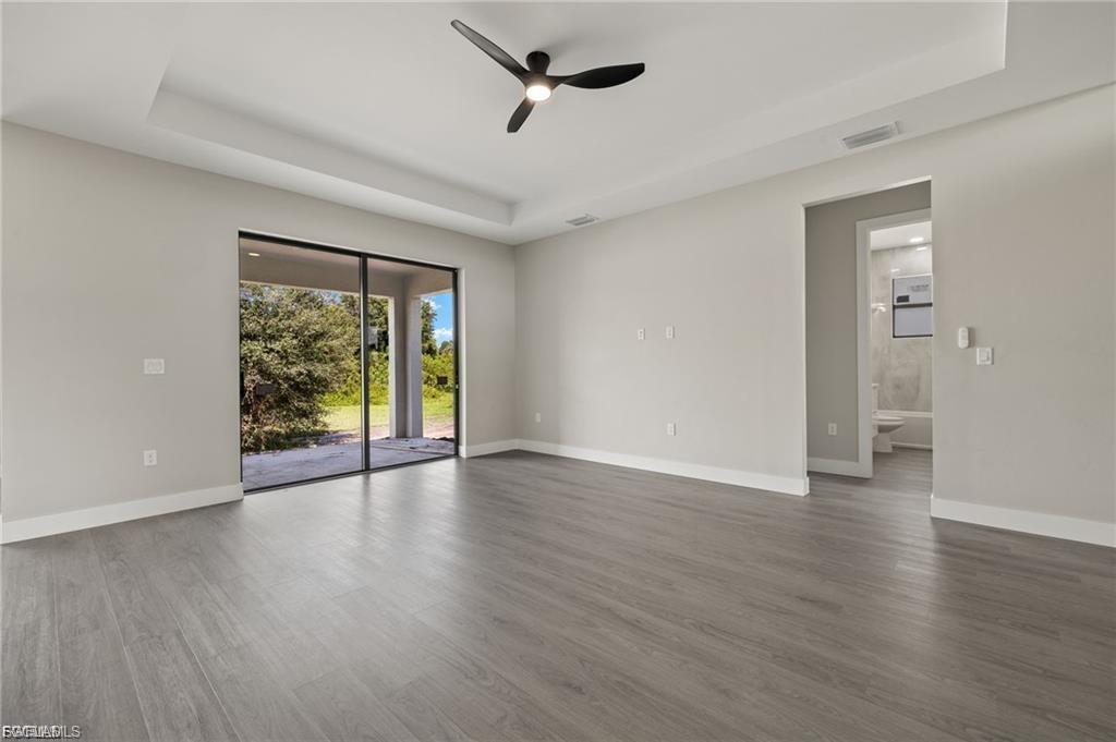 Empty room with a tray ceiling, a ceiling fan, and dark wood-style flooring