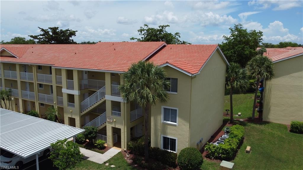 Multi-story building featuring a terra cotta tile roof, stucco exterior, multiple private balconies, external staircases, and a covered parking structure