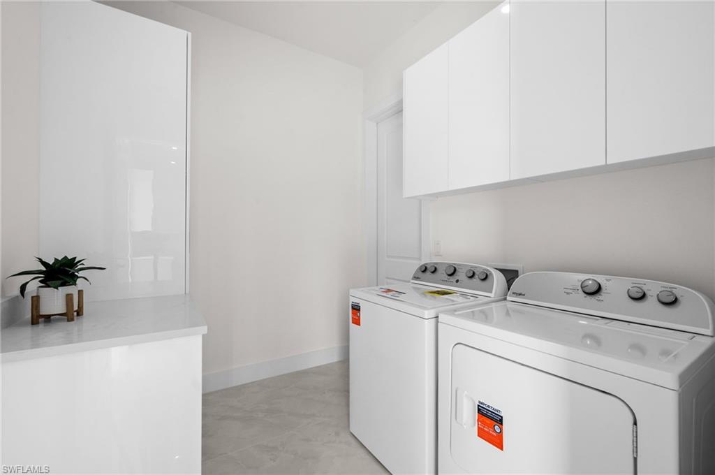 Modern utility space featuring a neutral color palette, stone-finish countertops, wall-mounted cabinetry, and a full-size washer and dryer set