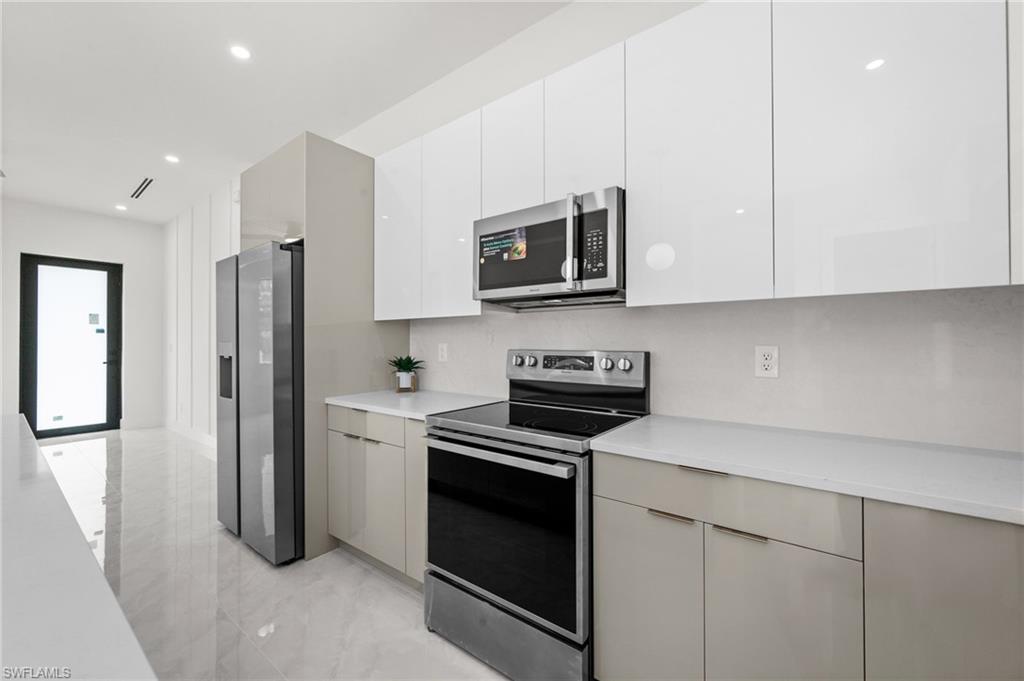 Modern kitchen featuring white glossy upper cabinetry, light gray base cabinetry, stainless steel appliances, and white countertops