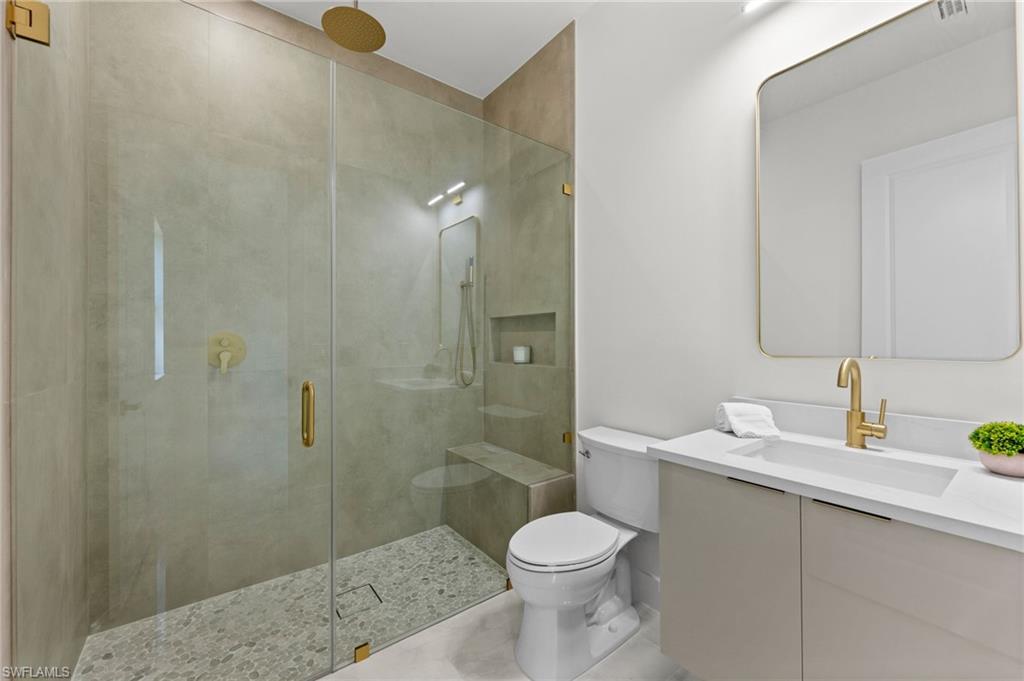 Contemporary bathroom featuring a frameless glass shower enclosure with gold-tone fixtures, a built-in shower bench, and pebble tile flooring