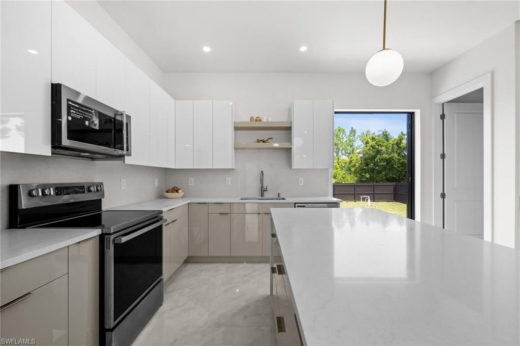 Modern kitchen featuring a large central island with a light-toned countertop, stainless steel appliances, gloss-finish cabinetry, a built-in microwave, and a glass door leading to the backyard