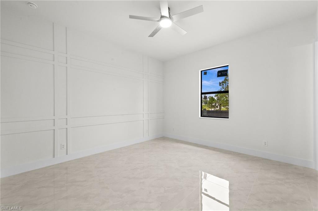 Spacious room featuring light-toned tile flooring, a contemporary ceiling fan, and decorative wall molding