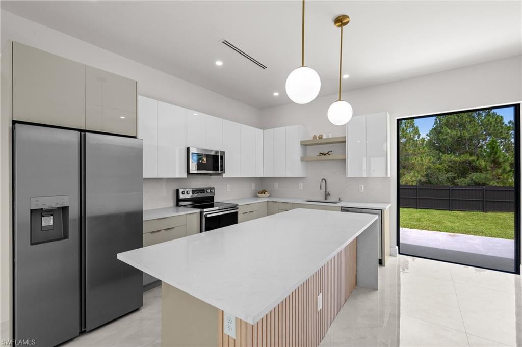 Modern kitchen featuring a spacious island with a light countertop, stainless steel appliances, white and gray cabinetry, and a sliding glass door opening to a private backyard