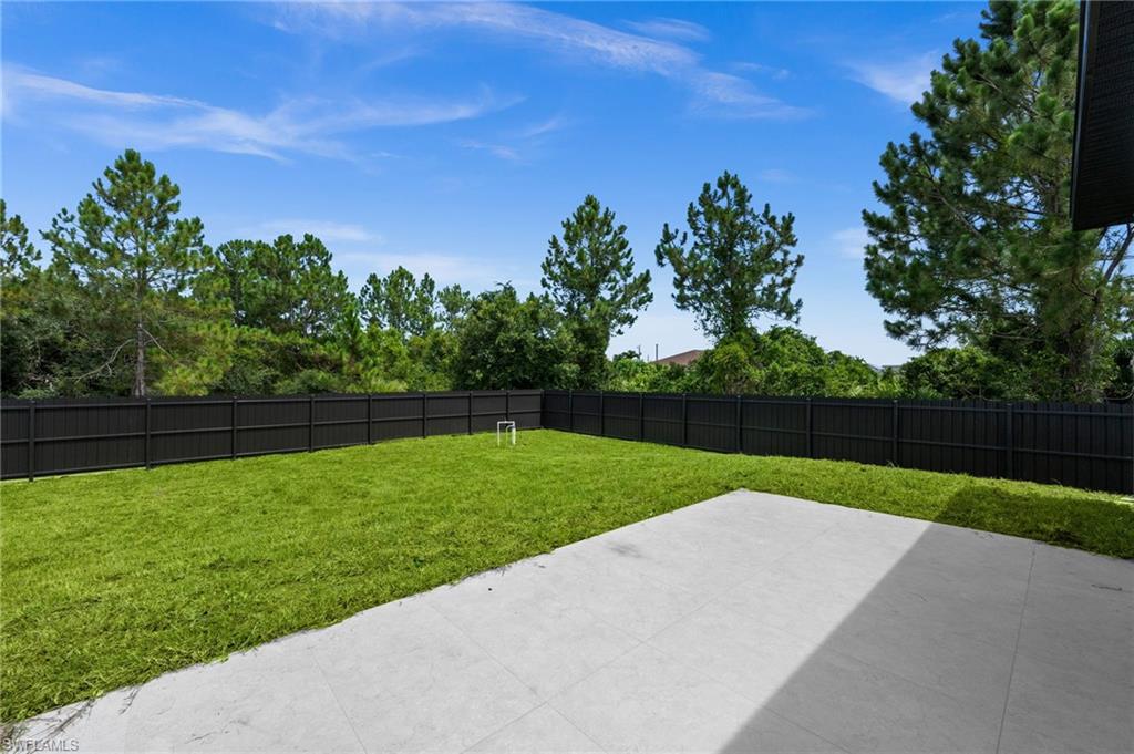 Expansive backyard featuring a large concrete patio, lush green lawn, and a dark privacy fence