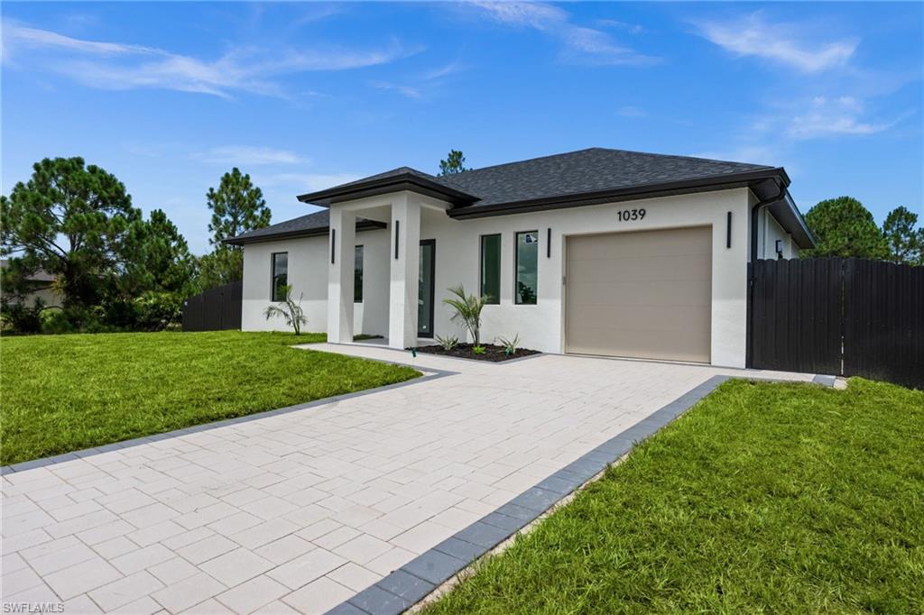 Modern exterior featuring a light stucco facade, dark trim, a stone paver driveway, and an attached garage
