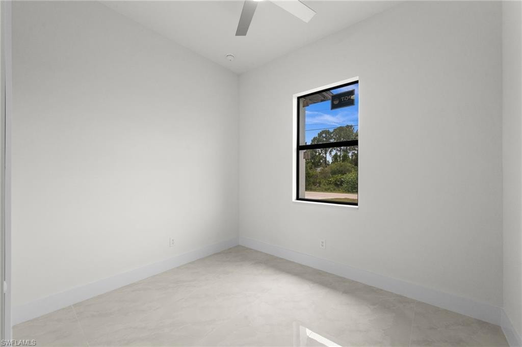 Room featuring light-toned tile flooring, clean white walls, a single window with dark trim, and a ceiling fan with integrated lighting