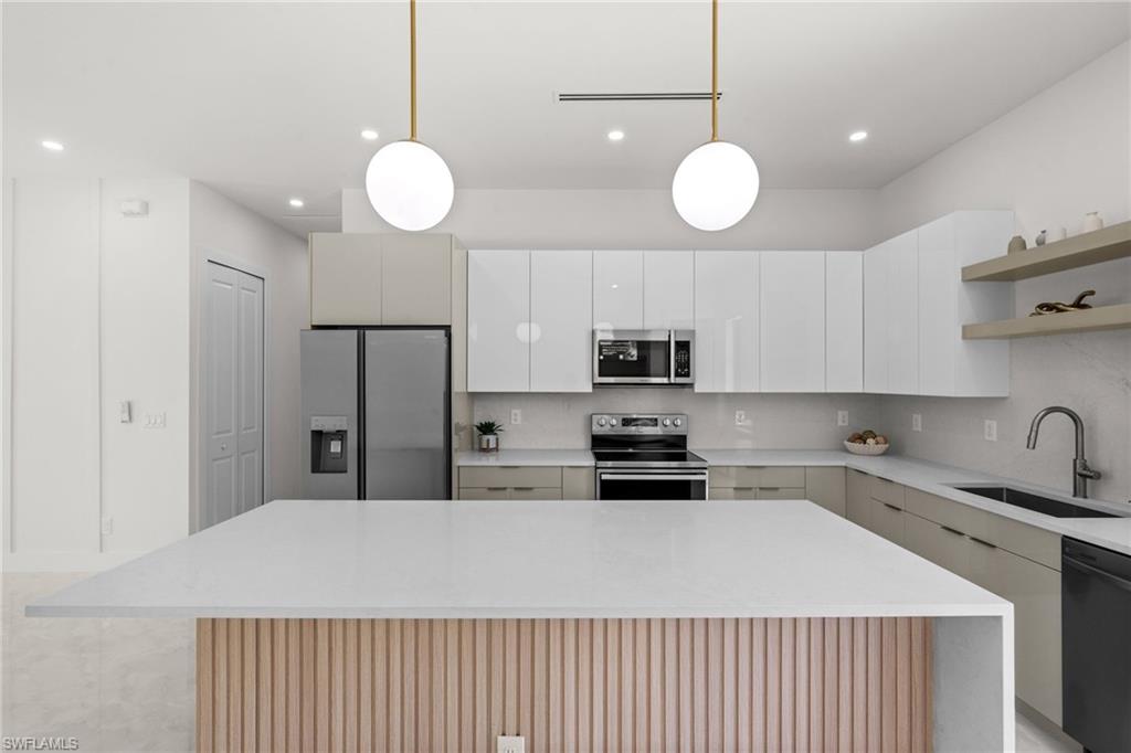Kitchen featuring a center island with slatted wood paneling and a light-toned countertop, stainless steel appliances, white upper cabinetry, and open shelving