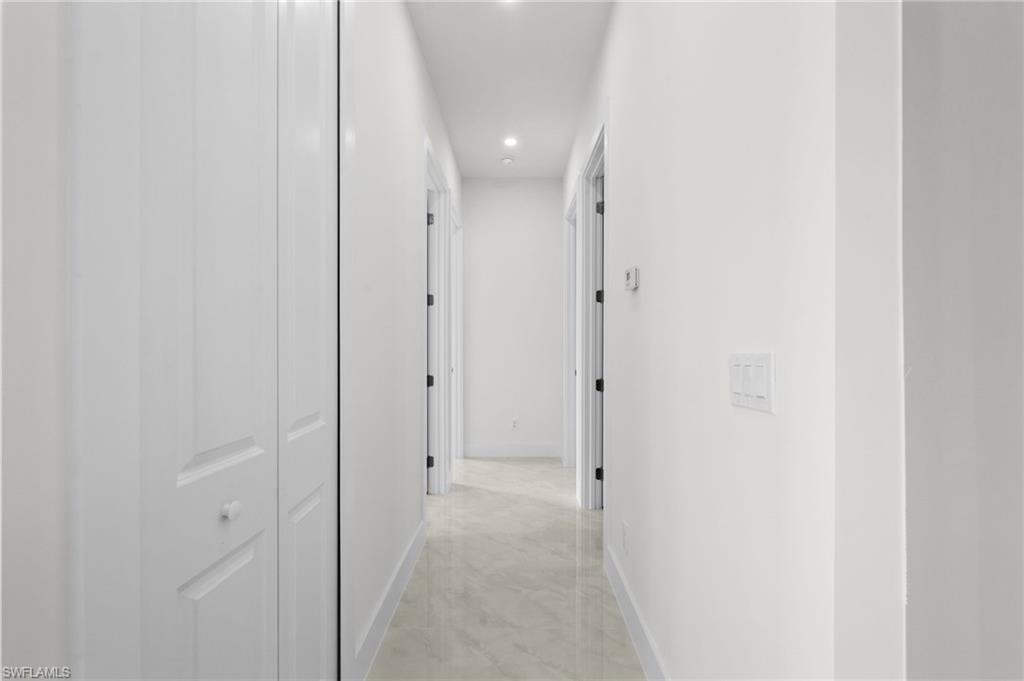 Bright hallway featuring clean white walls, recessed lighting, and light-toned tile flooring