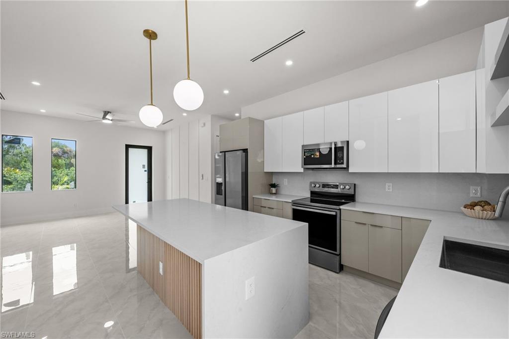 Modern kitchen featuring a waterfall island with wood slat detail, polished tile flooring, white flat-panel cabinetry, stainless steel appliances, and pendant lighting