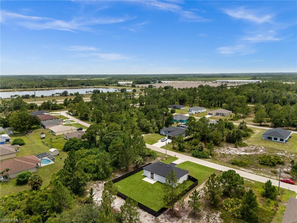 Aerial perspective featuring a single-story residence with a black roof and white exterior, surrounded by a manicured lawn and black perimeter fencing