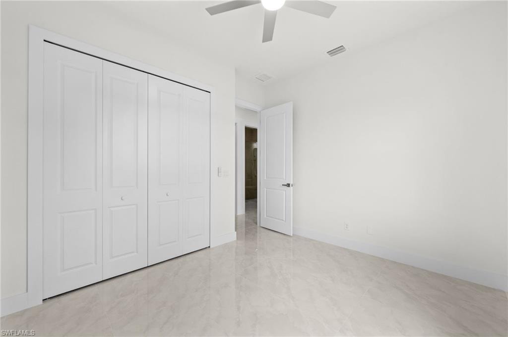 Bright room featuring a ceiling fan, white paneled bifold closet doors, a white paneled door, and large format tile flooring
