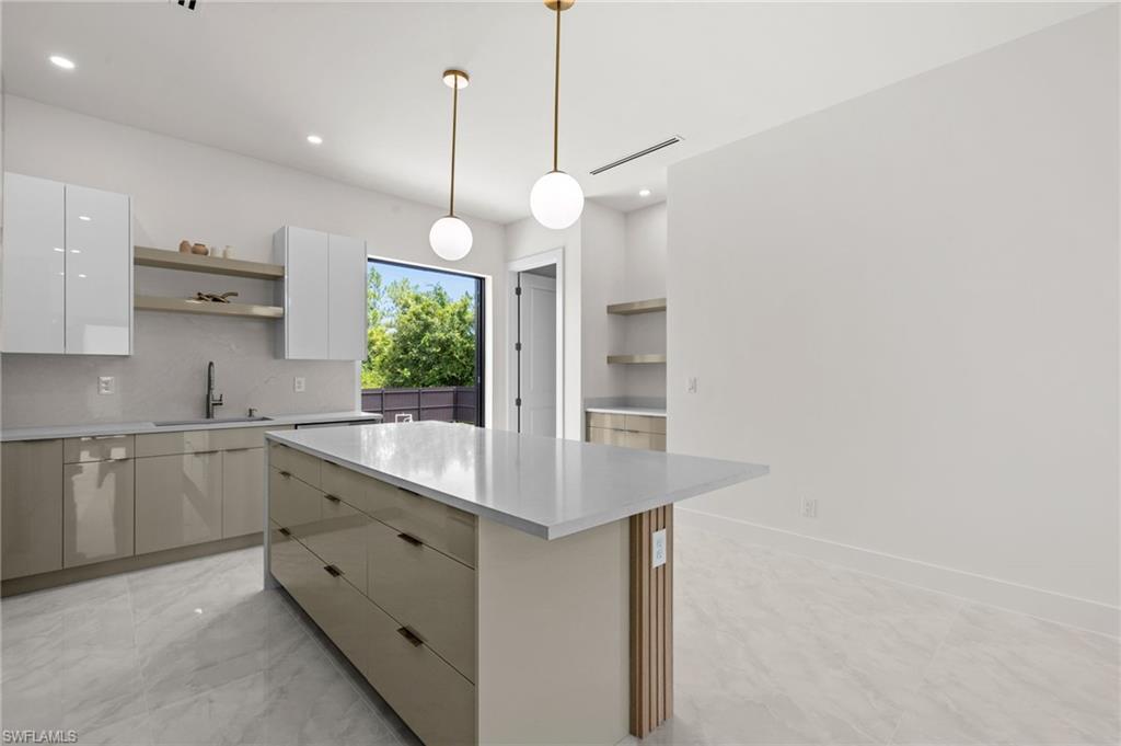 Modern kitchen featuring a spacious center island with a light-toned countertop, sleek cabinetry with an integrated sink, polished tile flooring, pendant lighting fixtures, and open shelving