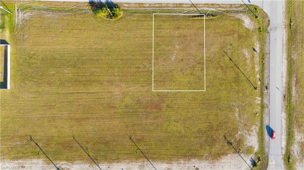 Expansive lot with a rectangular outline, featuring a grassy terrain and bordering a paved road