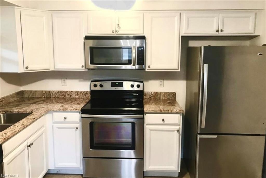 Kitchen featuring appliances with stainless steel finishes, white cabinets, and light stone countertops
