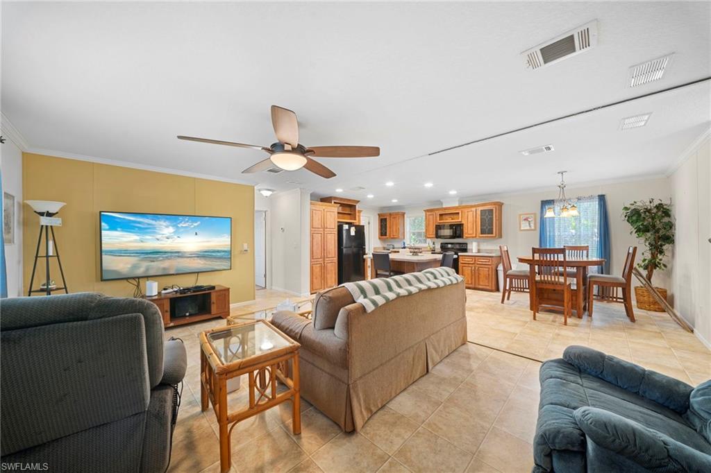 Open-concept interior featuring tile flooring, a living area with a ceiling fan, a kitchen with wood cabinetry and black appliances, and a dining area with a chandelier
