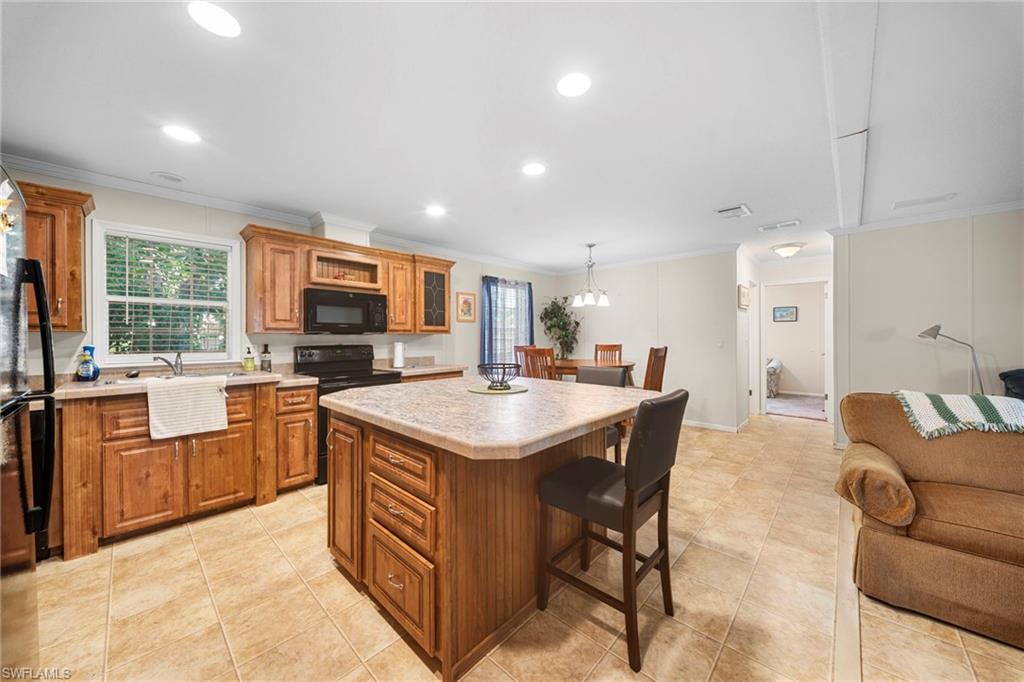 Open-concept kitchen featuring wood cabinetry, stone-finish countertops, black appliances, a central island with seating, and tile flooring