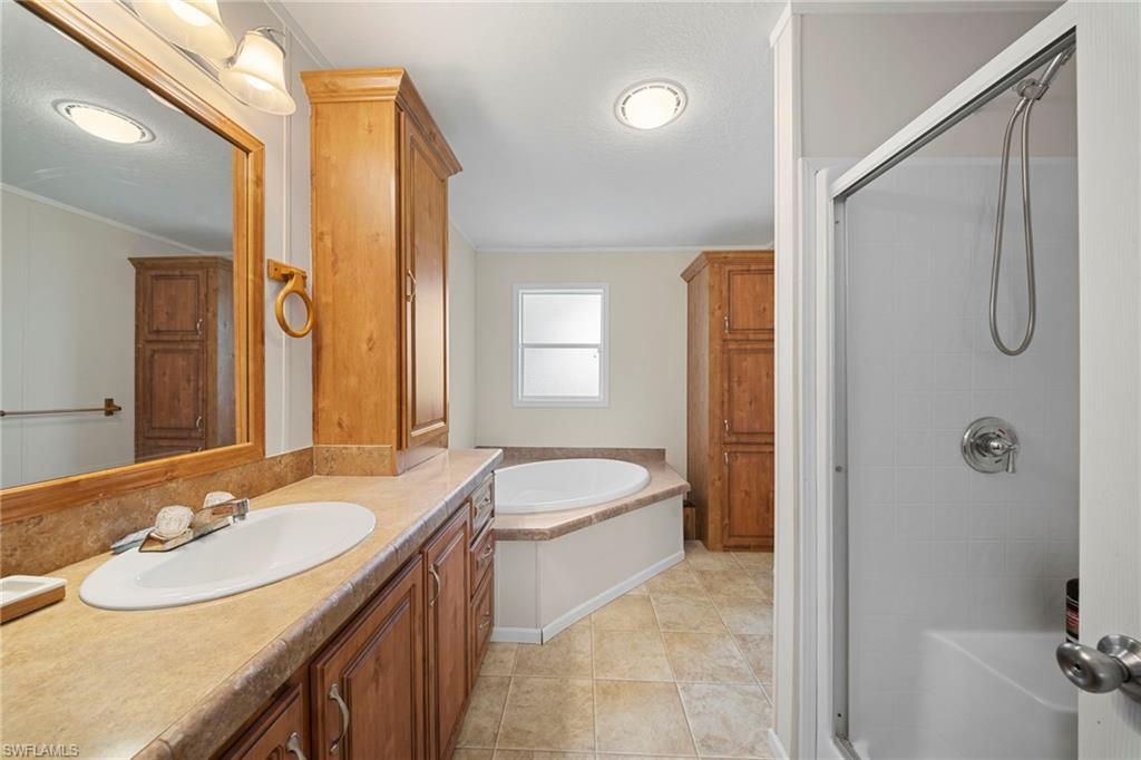 Bathroom featuring a built-in jetted tub, a separate shower enclosure with a glass door, a single vanity with an integrated sink, and ample storage provided by wood-finish cabinetry