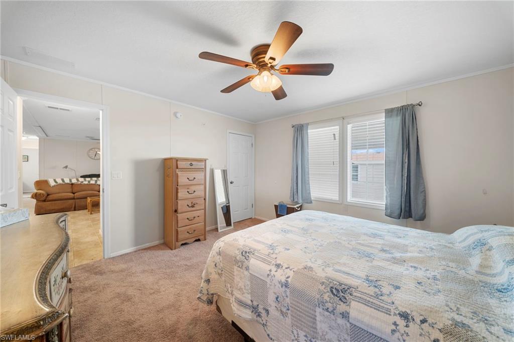Carpeted bedroom featuring a ceiling fan with light fixture, white trim, and two windows with blinds