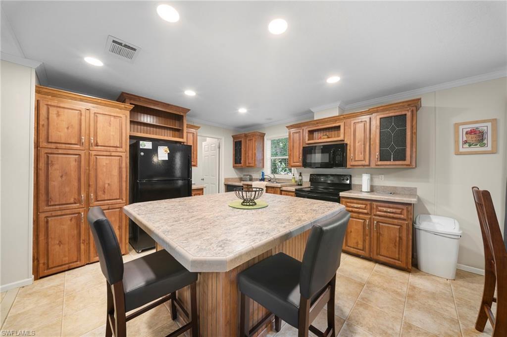 Kitchen featuring wood cabinetry, a central island with seating, black appliances, recessed lighting, and tile flooring