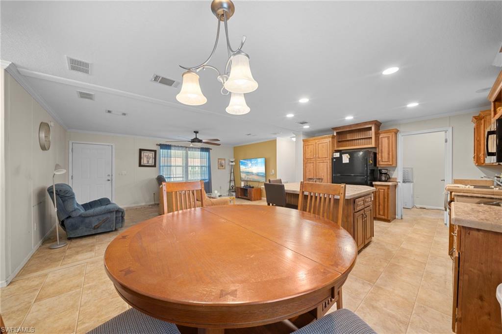 Open-concept living space with tile flooring, a dining area featuring a pendant light fixture, a kitchen island with storage, wood cabinetry, and a ceiling fan in the living room area