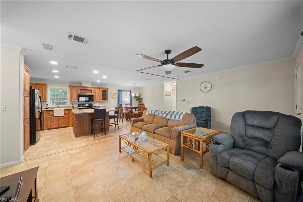 Open concept living area with tile flooring throughout, featuring a kitchen with wood cabinetry and black appliances, a dining area, and a living room with a ceiling fan