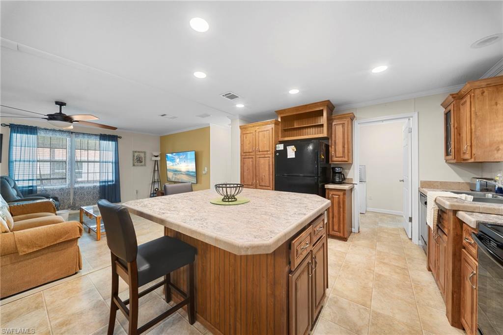 Kitchen featuring a central island with countertop seating, wood-finish cabinetry, black appliances, and tile flooring