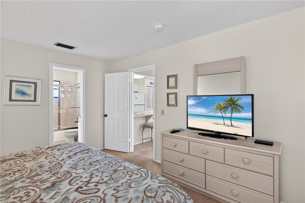 Primary bedroom featuring light carpet, a textured ceiling, freestanding refrigerator, and ensuite bath
